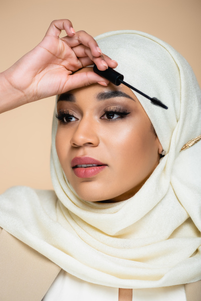 young muslim woman in hijab holding mascara brush isolated on beige - Photo, Image