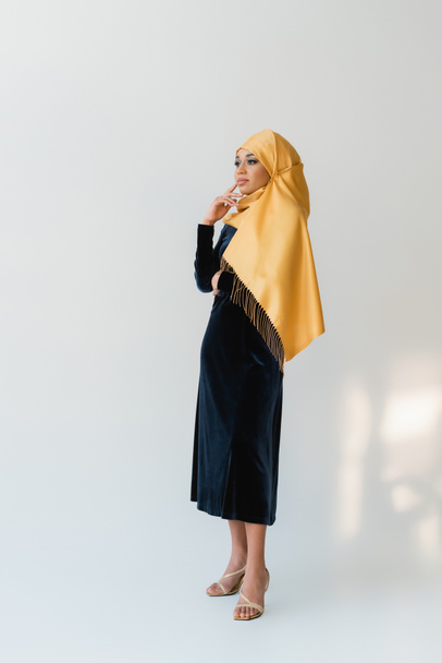full length of dreamy muslim woman in hijab and velvet blue dress on white - Foto, imagen
