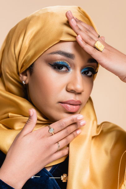 muslim woman in yellow hijab with bright makeup and golden rings looking at camera isolated on beige - Foto, imagen