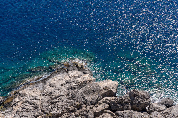 An aerial view of the rocky cliffs on the Aegean sea under the blue sky in Greece - Photo, Image