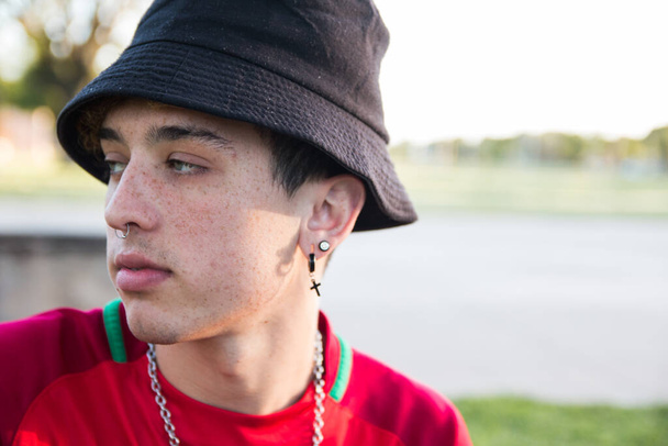A portrait of a cool young Argentine man with earrings and a piercing wearing a bucket hat outdoors - Fotó, kép