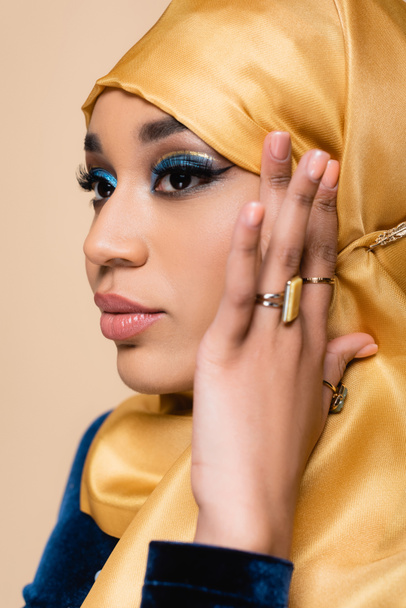 pretty muslim woman in yellow hijab with golden rings on fingers posing isolated on beige - Foto, imagen