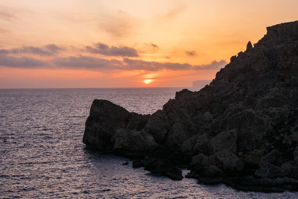 Sunset on a beautiful spring day as seen from Anchor Bay, Mellieha, Malta. The sun setting over the horizon with some clouds and calm sea. - 写真・画像