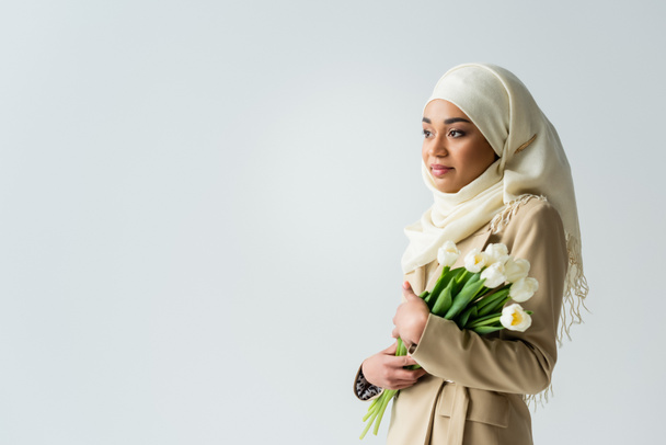 mujer bastante musulmana en hijab blanco sosteniendo tulipanes aislados en gris - Foto, imagen