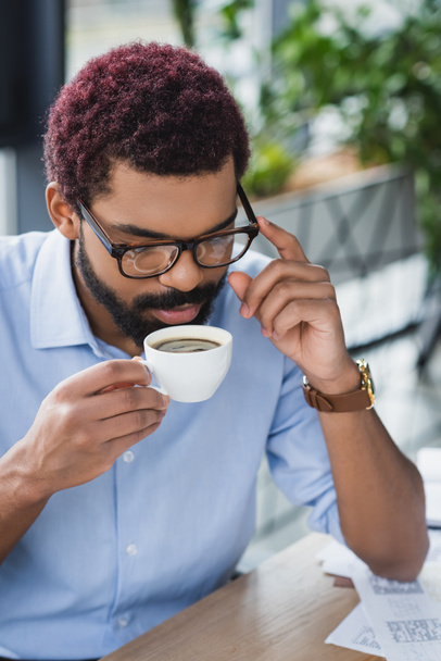 African american businessman in eyeglasses holding cup of coffee in office  - Фото, изображение
