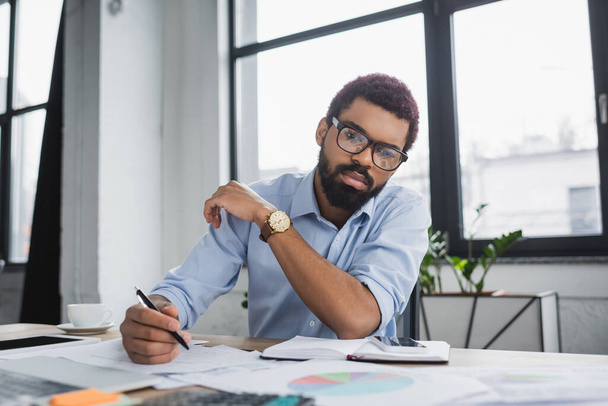 African american manager holding pen near papers and gadgets in office - Foto, Bild