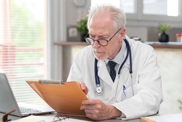 Médecin principal lisant un dossier clinique au cabinet médical - Photo, image