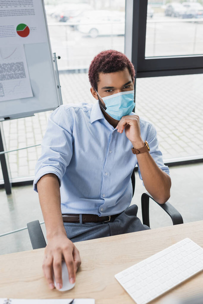 医療用マスクのアフリカ系アメリカ人マネージャーオフィスでフリップチャートの近くにコンピュータマウスを使用して  - 写真・画像