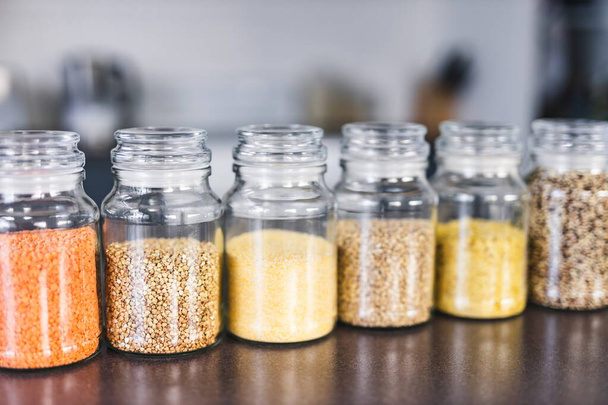 clear pantry jars with different types of grains and legumes including quinoa  lentils buckwheat and barley on benchtop with kitchen bokeh, simple ingredients concept - Foto, Bild
