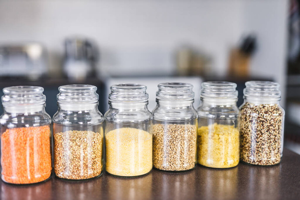 clear pantry jars with different types of grains and legumes including quinoa  lentils buckwheat and barley on benchtop with kitchen bokeh, simple ingredients concept - Zdjęcie, obraz