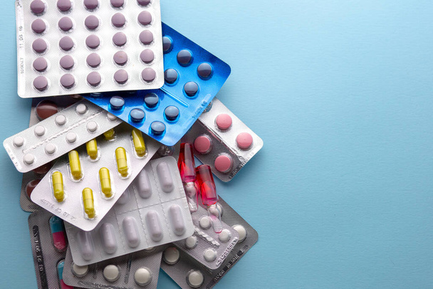 Overdose of pills. Medicines. Multicolored Pills Medicines Many Multicolored Pills Hands Background MedicinesFlu treatment. Coronavirus treatment. Pharmacy. Medicines in the public domain. Vitamins. Drugs. Colored slippers on a blue background. - Photo, Image