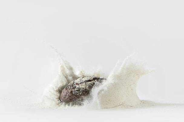 Minimalistic picture - rye bread falling into flour on a white background - Foto, Imagem