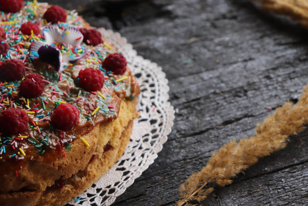 A closeup of a delicious homemade cake with berries and sprinkles on a wooden surface - Фото, зображення