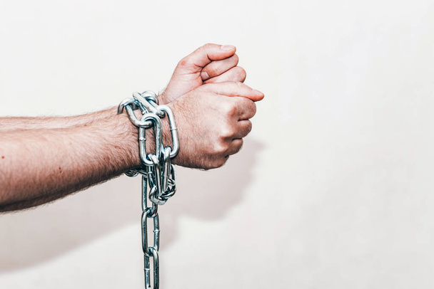 Men 's hand in a steel chain.Steel chains in the hands of man on a gray wall background.Toned.Tonseup, selective focus.Copy space. - Фото, изображение
