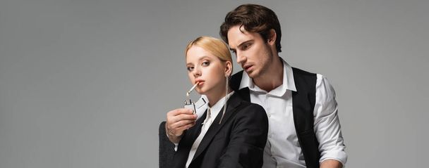 stylish man lightening cigarette of blonde woman looking at camera isolated on grey, banner - Foto, afbeelding