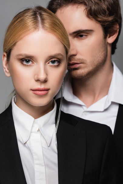elegant blonde woman looking at camera near blurred young man isolated on grey - Foto, immagini