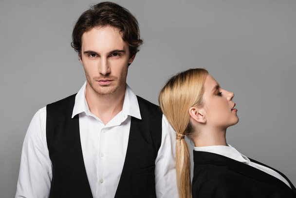 blonde woman leaning on shoulder of elegant man looking at camera isolated on grey - Foto, afbeelding