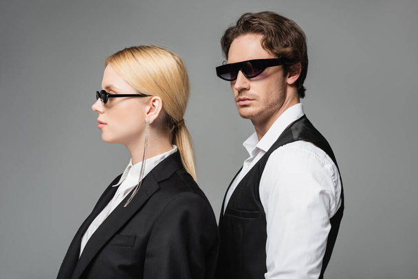 blonde woman and brunette man in dark sunglasses and elegant clothes posing isolated on grey - 写真・画像