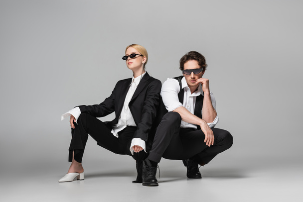 elegant couple in black suits and dark sunglasses posing on grey - Fotografie, Obrázek