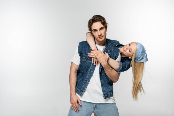 cheerful young woman embracing man in denim clothes standing isolated on white - Foto, immagini