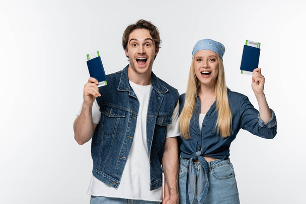 thrilled couple in denim clothes holding hands and travel documents isolated on white - Fotografie, Obrázek