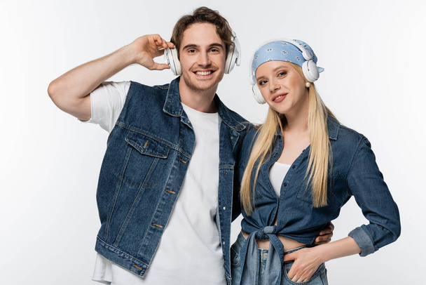 fröhliches Paar in Jeanskleidung, das Musik in drahtlosen Kopfhörern isoliert auf weißem Grund hört - Foto, Bild