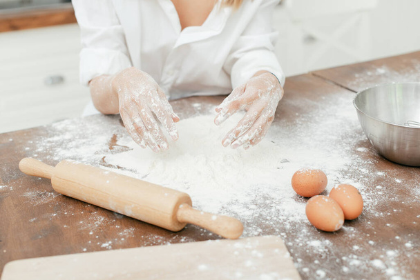 girl in the kitchen sculpts dough hands and table in white flour close-up - Фото, изображение