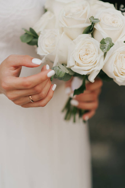 beautiful wedding bouquet and hand of the bride with white manicure close up - Photo, Image