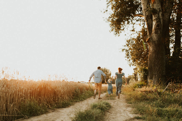 Parents and daughter relationship. Mom and dad hugs their kid. walking on a beautiful fiels. Close up of running kid and parents holding hands. Freedom and love concept. Happy family in a nature - Fotografie, Obrázek