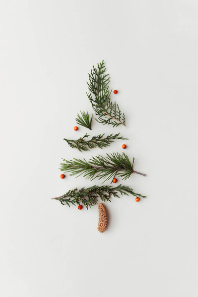 Χριστουγεννιάτικο δέντρο φτιαγμένο από φύλλα, κλαδιά και μούρα. Πρωτοχρονιά ή ιδέα διακοπών. Minimal επίπεδη θέσει δημιουργική ιδέα. - Φωτογραφία, εικόνα