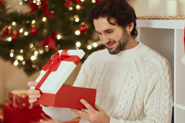 Homme avec présent dans la boîte cadeau près de l'arbre de Noël à la maison - Photo, image