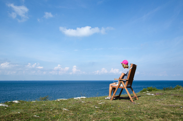 Nainen katselee rantaviivaa tuolilta
 - Valokuva, kuva