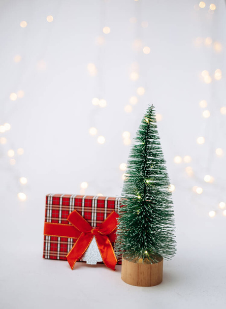 Beyaz arka planda yeni yıl hediyesi olan küçük yapay bir Noel ağacı ve mesaj için yeri olan bir bokeh. - Fotoğraf, Görsel