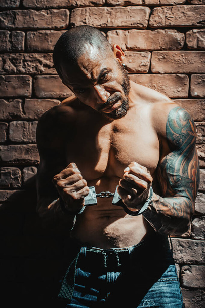 Um bandido ou violador em tatuagens é preso em confinamento solitário. Mãos algemadas. - Foto, Imagem