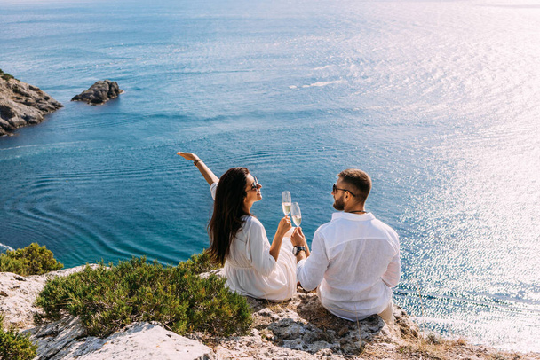 A couple in love celebrates their engagement on the seashore. A beautiful couple drinks champagne by the sea. Honeymoon trip. Lovers on the beach. Wedding travel. Couple on vacation. Copy space - Foto, Imagem