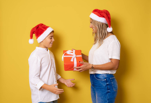 Portret młodej matki i syna w kapeluszu z pudełkiem prezentów na żółtym tle - Zdjęcie, obraz