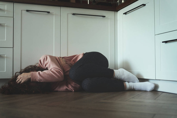Młoda kobieta z zakrytą twarzą leżąca na podłodze w kuchni - Zdjęcie, obraz