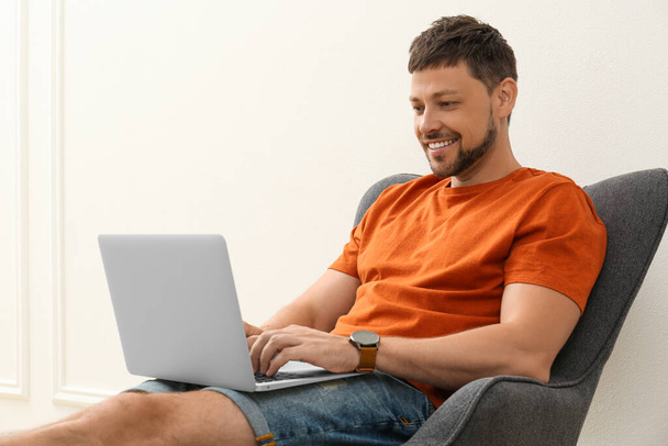 Happy man using laptop in armchair indoors. Internet shopping - Foto, immagini