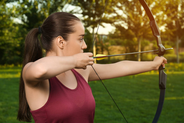 Woman with bow and arrow practicing archery in park - Fotoğraf, Görsel