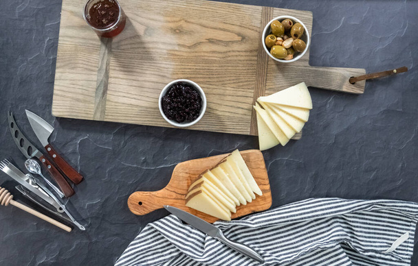 Flat lay. Arranging cheese, crackers, and fruit on a wood cutting board to create appetizer cheese board. - Photo, Image