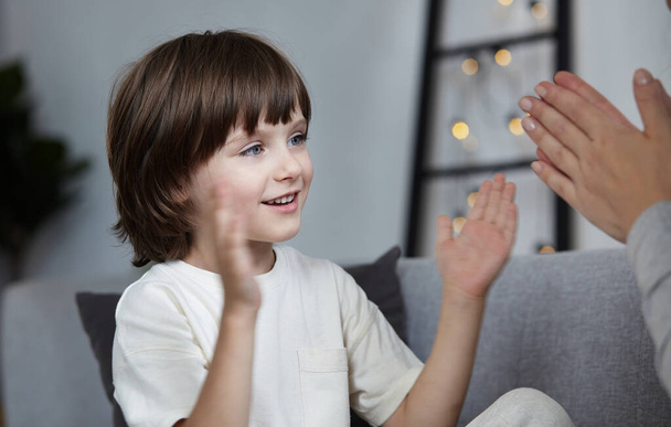 Female parent playing with male kid clapping hands at home. Happy woman spending time with son - Photo, Image