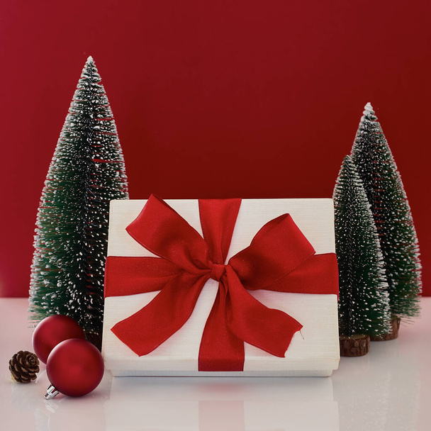 Σύνθεση με κουτί δώρου Χριστουγέννων με διακόσμηση χριστουγεννιάτικου δέντρου σε κόκκινο φόντο - Φωτογραφία, εικόνα