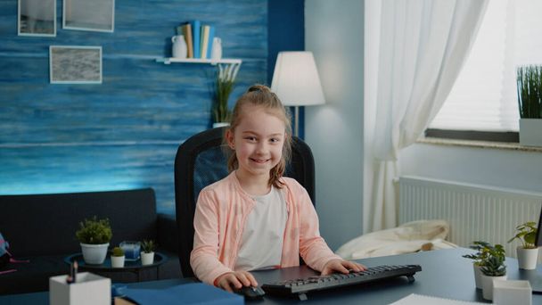 Portret van een kind achter een bureau met computer voor online lessen - Foto, afbeelding