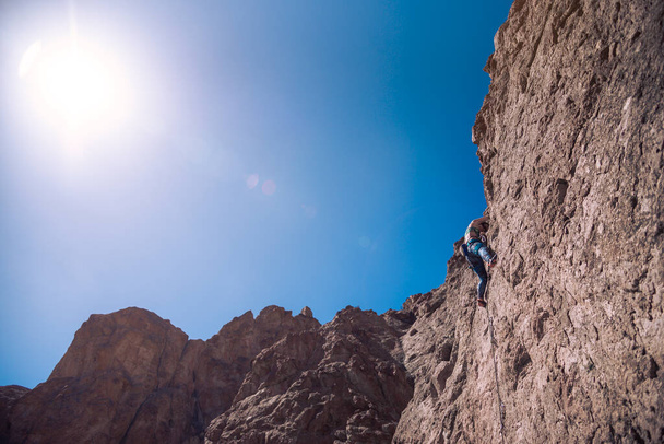 Female climber. Young adult fit woman climbing with rope a stone rock wall at sunny day. Concept of adventure and extreme sport outdoors. Climbing equipment and sportswear - Photo, Image