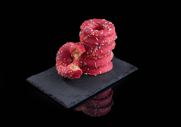 primer plano de columna de donuts rosas encima de un plato sobre fondo negro e instrumental medico dentista - Fotó, kép