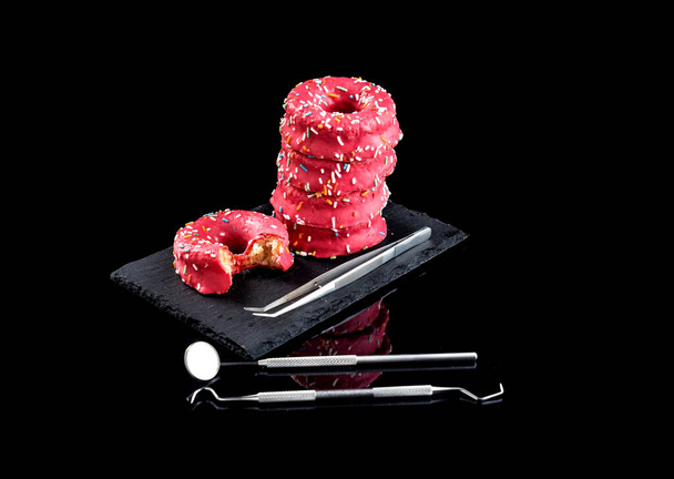 İlk plano de columna de donuts rosas encima de un plato ayık fondo negro ve enstrümantal medio dişçi - Fotoğraf, Görsel