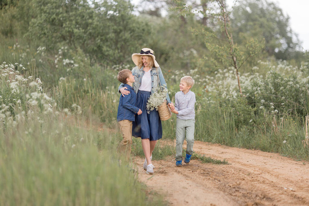 Mother in a straw hat, denim dress with young sons walking through the woods .Outdoor spring leisure concept - Фото, зображення