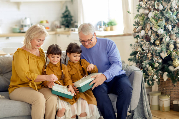 Cute granddaughter twins unwrap presents with grandma and grandpa . Christmas season. Family tradition - Foto, Imagem