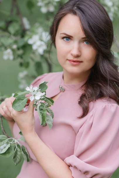 A beautiful woman in a blue dress is standing near a blooming apple tree. Pregnant young happy women in bloom white garden. Pregnant woman in spring garden - Fotó, kép
