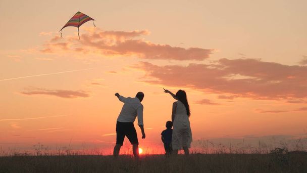 mom dad and kid launch flying kite into sky at sunset, happy family, childhood dream of flying, father, mother and child, travel together on vacation, teamwork, teach baby to play take care and love - Photo, Image